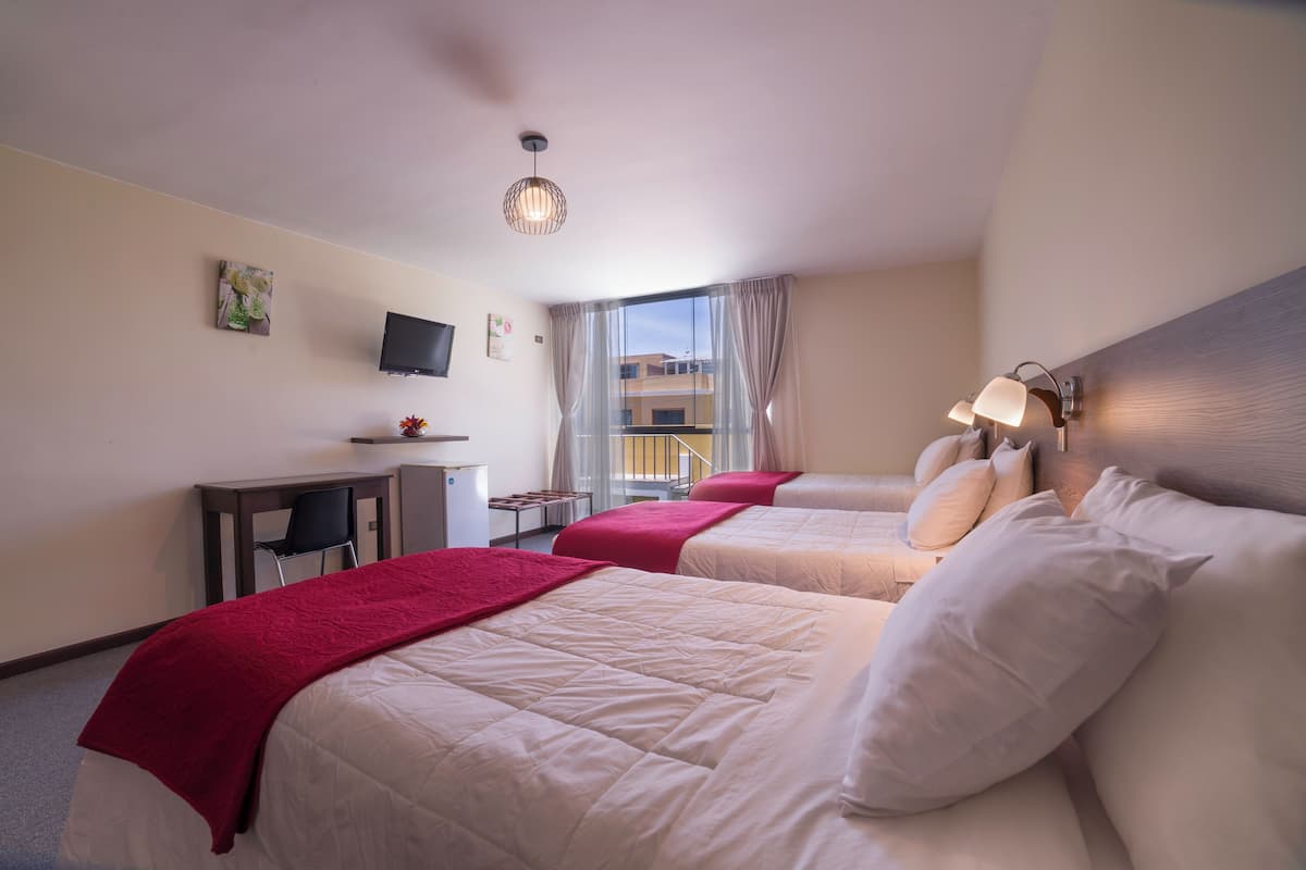 A hotel room with two beds, a desk, a chair, a TV, and a window with curtains.