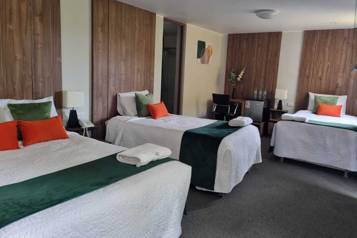 A hotel room with two beds, a desk, a chair, and a small kitchenette.