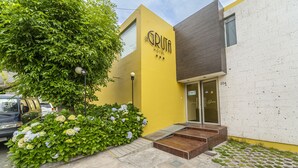 A hotel entrance with a yellow facade, a glass door, and a small set of wooden steps leading up to the entrance. - La Gruta (Arequipa)