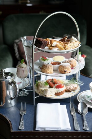 A three-tiered dessert stand with various pastries and desserts, a silver teapot, and a set of silverware on a table. - Station House Hotel (Kilmessan)