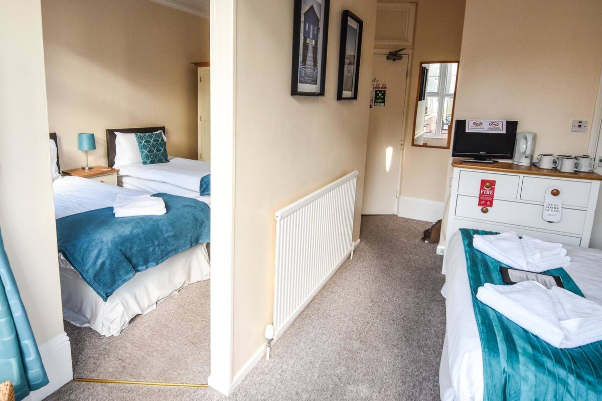 Une chambre d’hôtel avec deux lits, une commode, un radiateur et une fenêtre avec des rideaux.