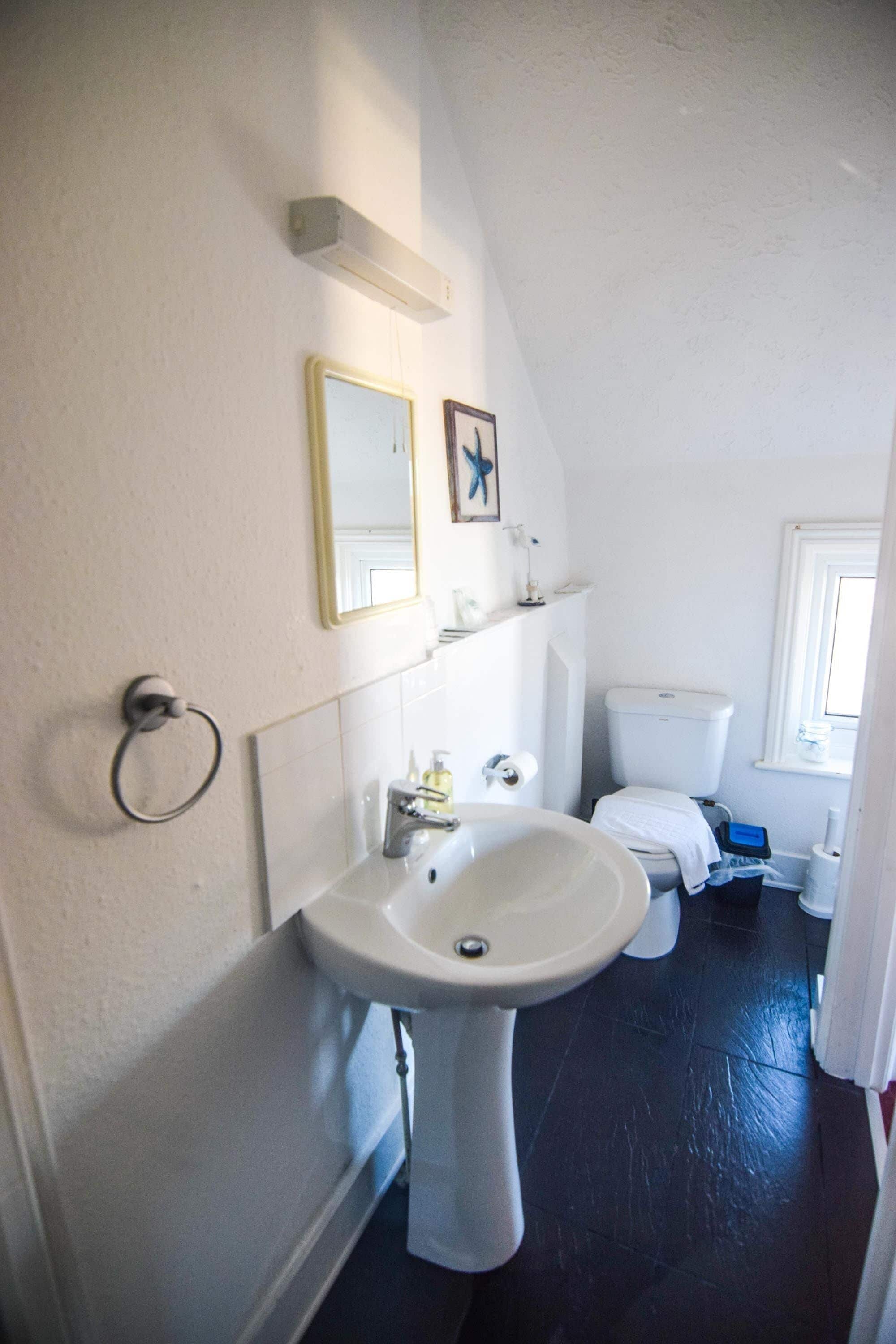 A bathroom with a pedestal sink, toilet, and a small window.