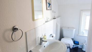 A bathroom with a pedestal sink, toilet, and a small window.