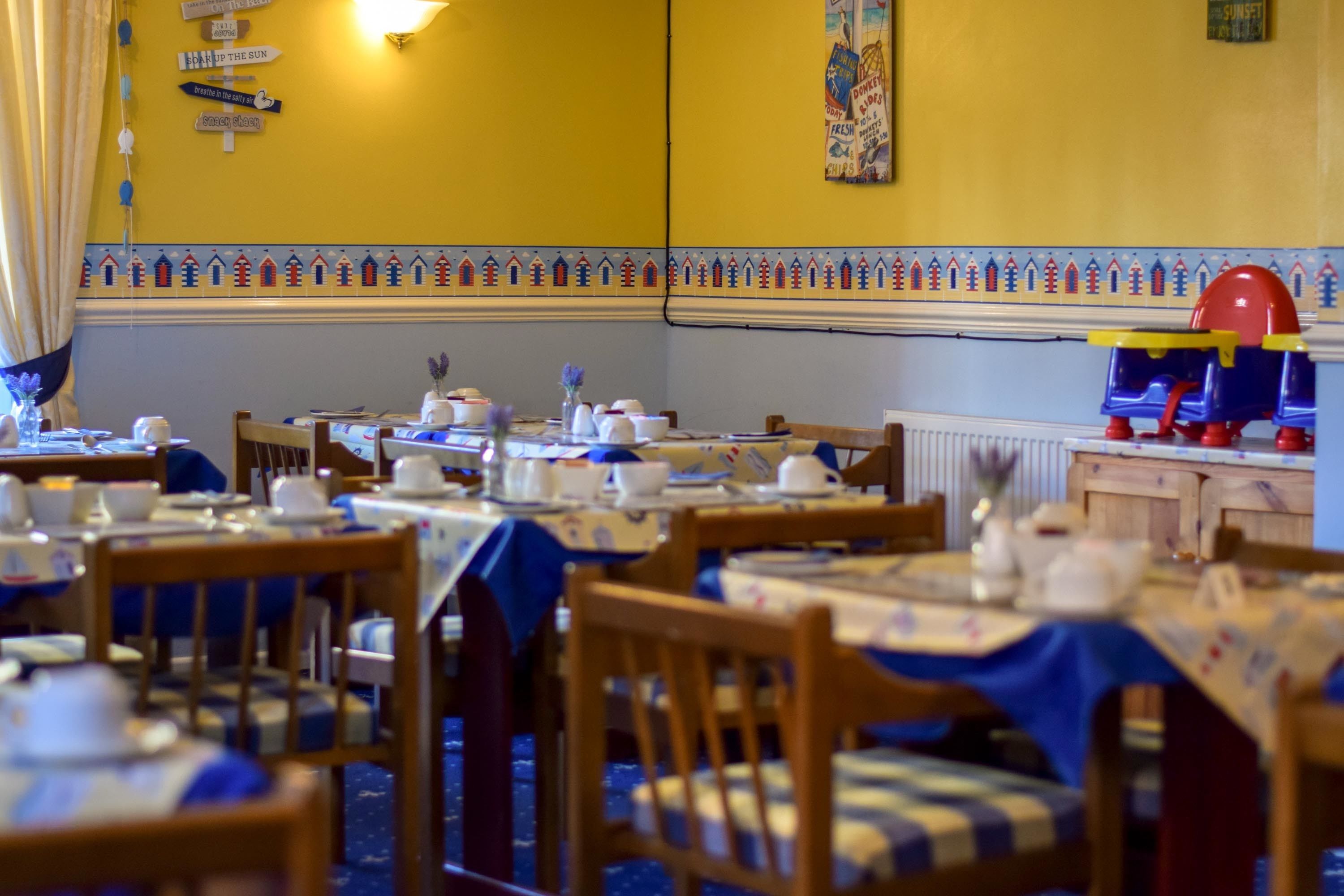 A dining area with tables set for service, wooden chairs, and a wall with decorative tiles and signs.