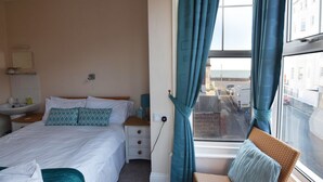 A hotel room with a bed, a bedside table with a lamp, a window with curtains, and a view of the street outside.