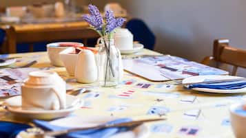 A dining table set with white ceramic dishes, a vase with purple flowers, and a colorful tablecloth.