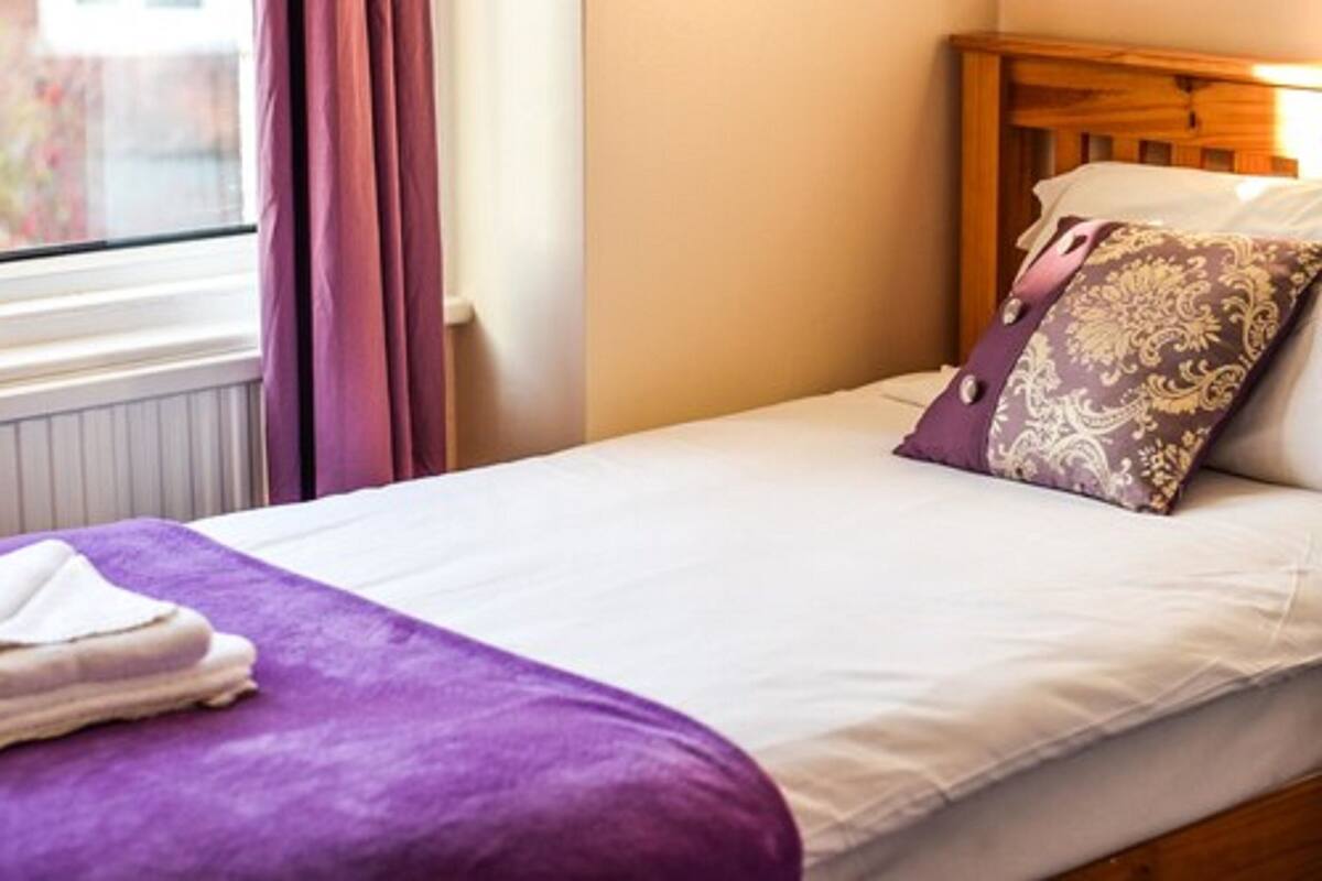 Un lit simple avec un matelas blanc, une couverture violette et un coussin décoratif.