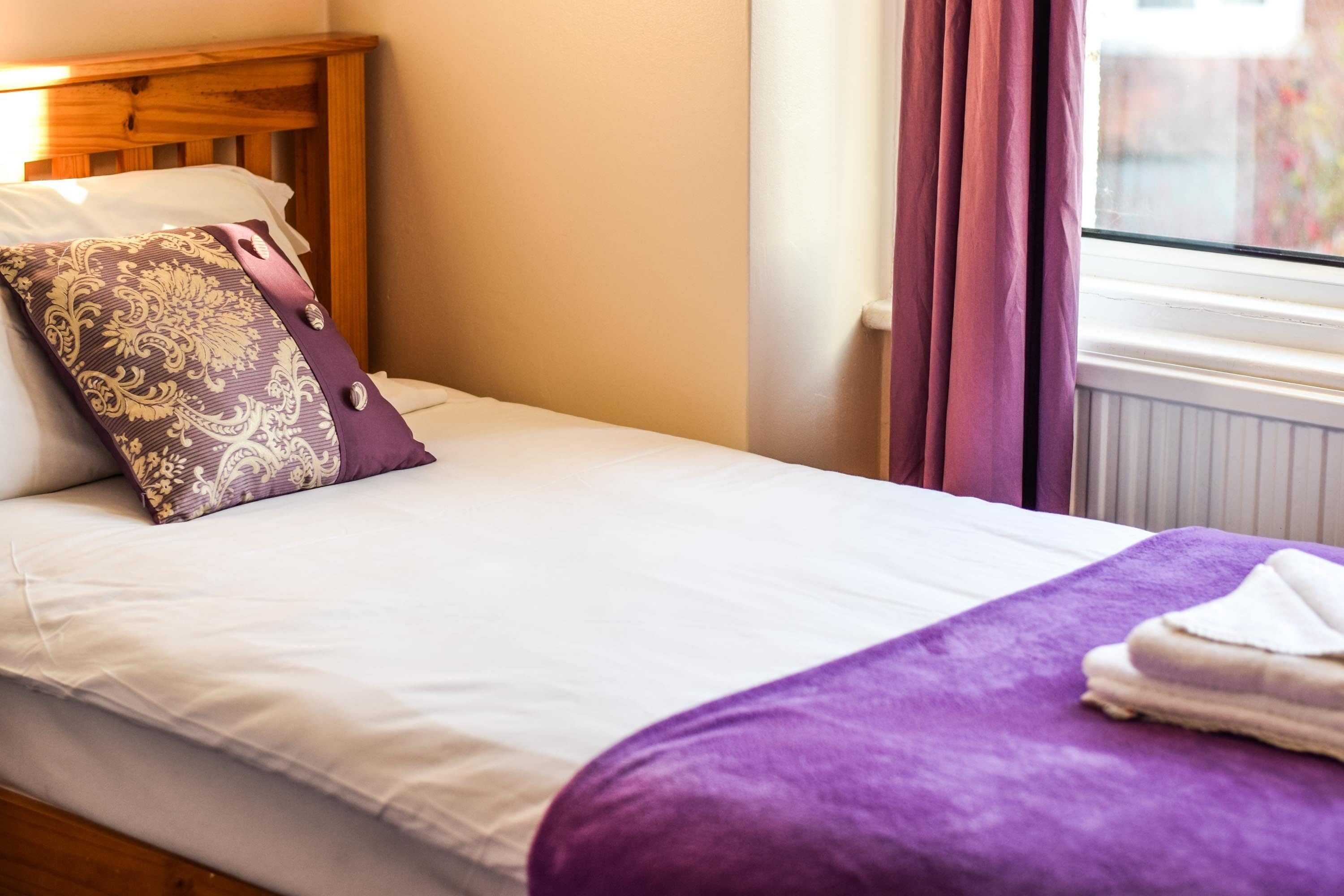 A neatly made bed with a purple blanket and a decorative pillow.