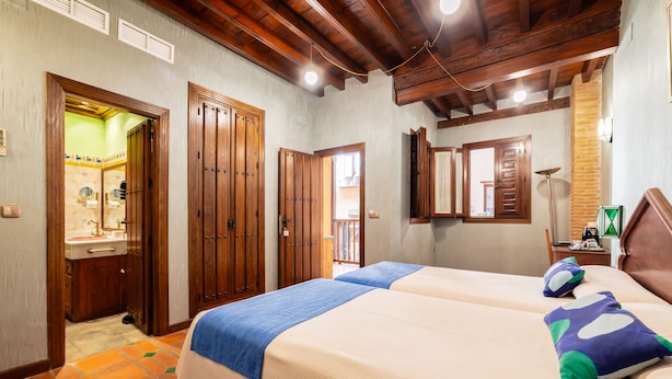 A hotel room with two beds, wooden doors, a bathroom with a sink, and a mirror. - Posada del Toro (Granada)