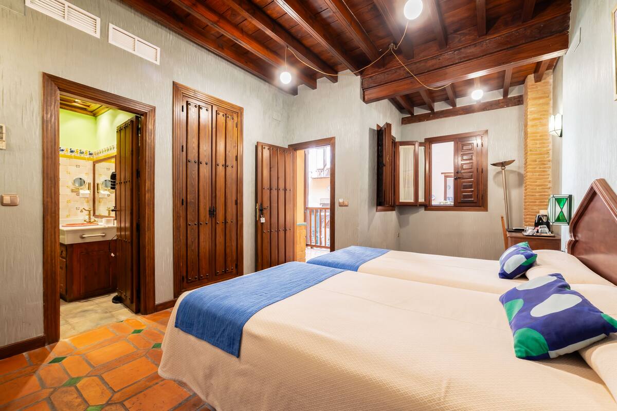 A hotel room with two beds, wooden doors, a bathroom with a sink, and a mirror.