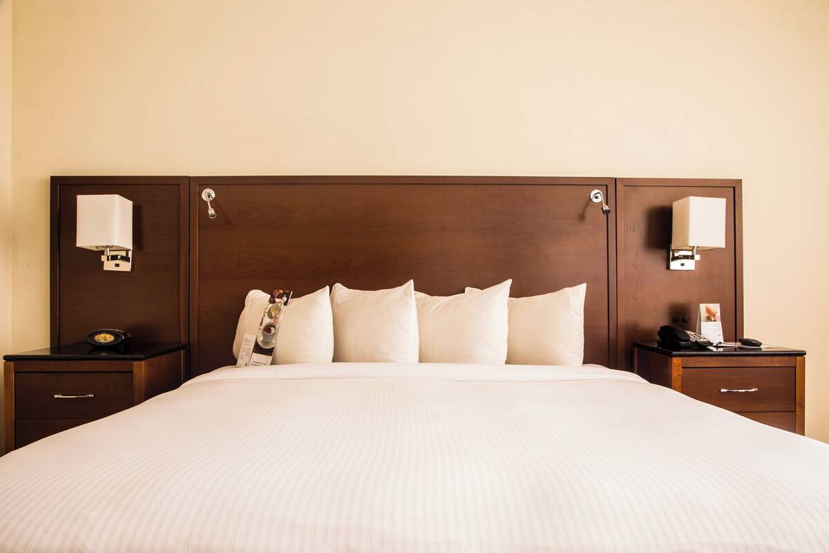 Une chambre d’hôtel avec un grand lit, deux tables de chevet, une tête de lit en bois et des lampes de chevet.