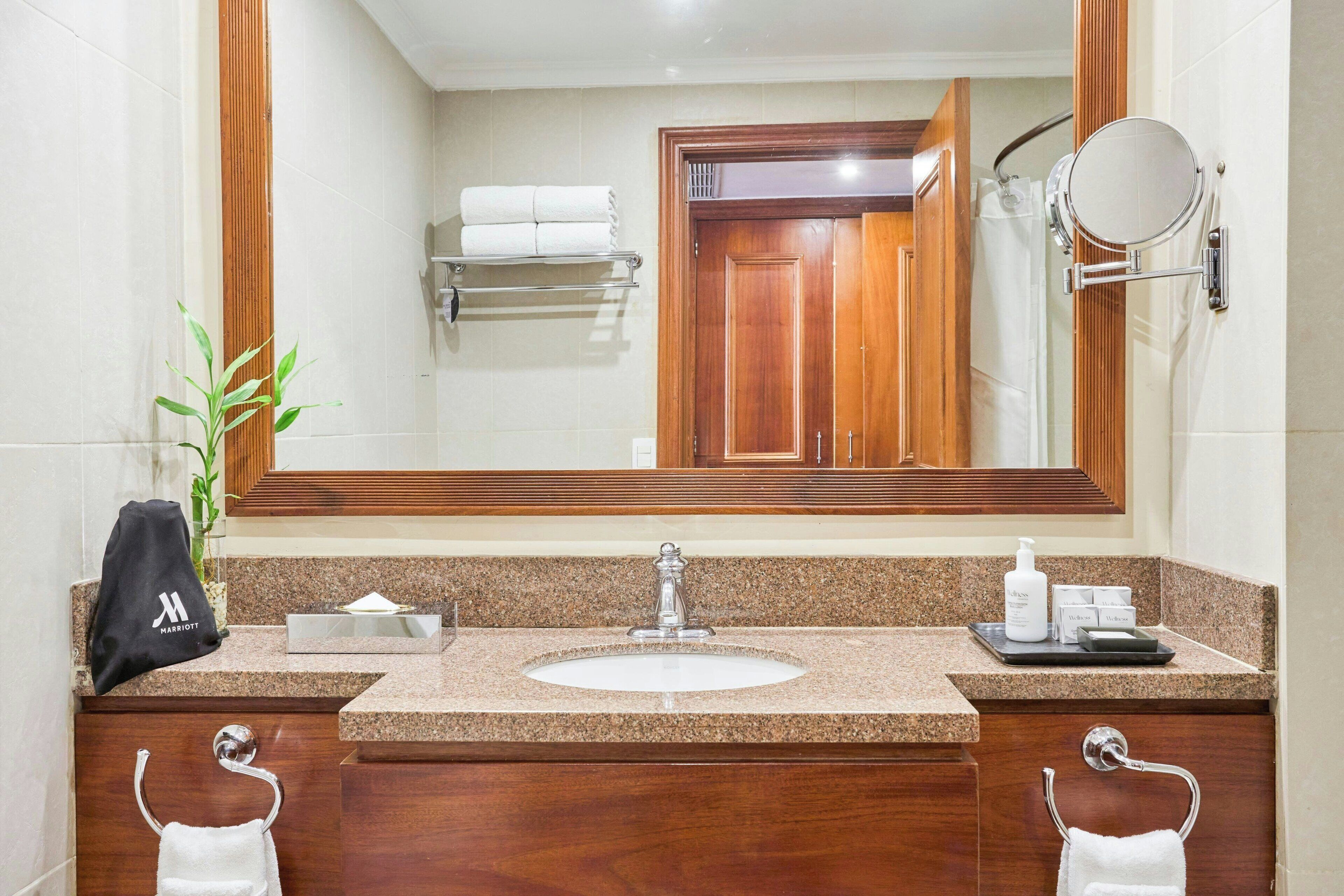 A hotel bathroom with a large mirror, a sink, and two towel racks.