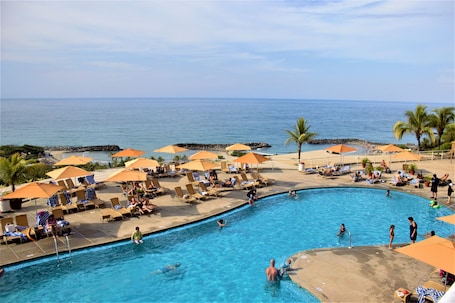 A pool area with lounge chairs and umbrellas, a clear view of the ocean, and a lifeguard tower.