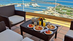 A balcony with wicker furniture, a table set with breakfast, and a view of a marina and coastline. - Venezuela Marriott Hotel Playa Grande (Urimare)