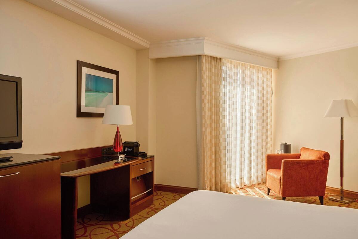 Une chambre d’hôtel avec un lit, un bureau, une chaise, une télévision et une fenêtre avec des rideaux.