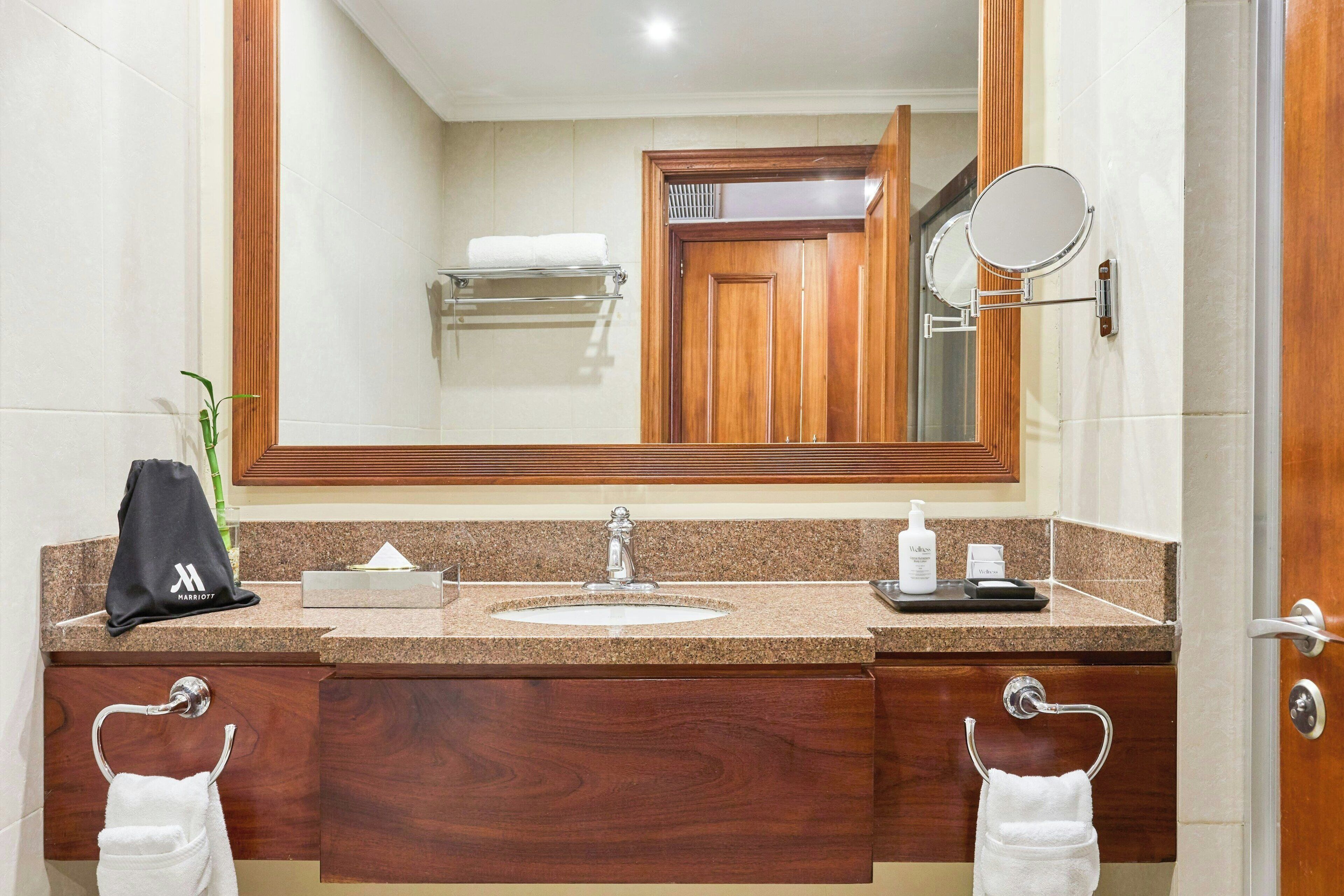 A hotel bathroom with a granite countertop, a sink, a mirror, and wooden cabinetry.