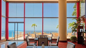 A dining area with a view of the ocean, featuring tables, chairs, and a vase with flowers. - Venezuela Marriott Hotel Playa Grande (Urimare)