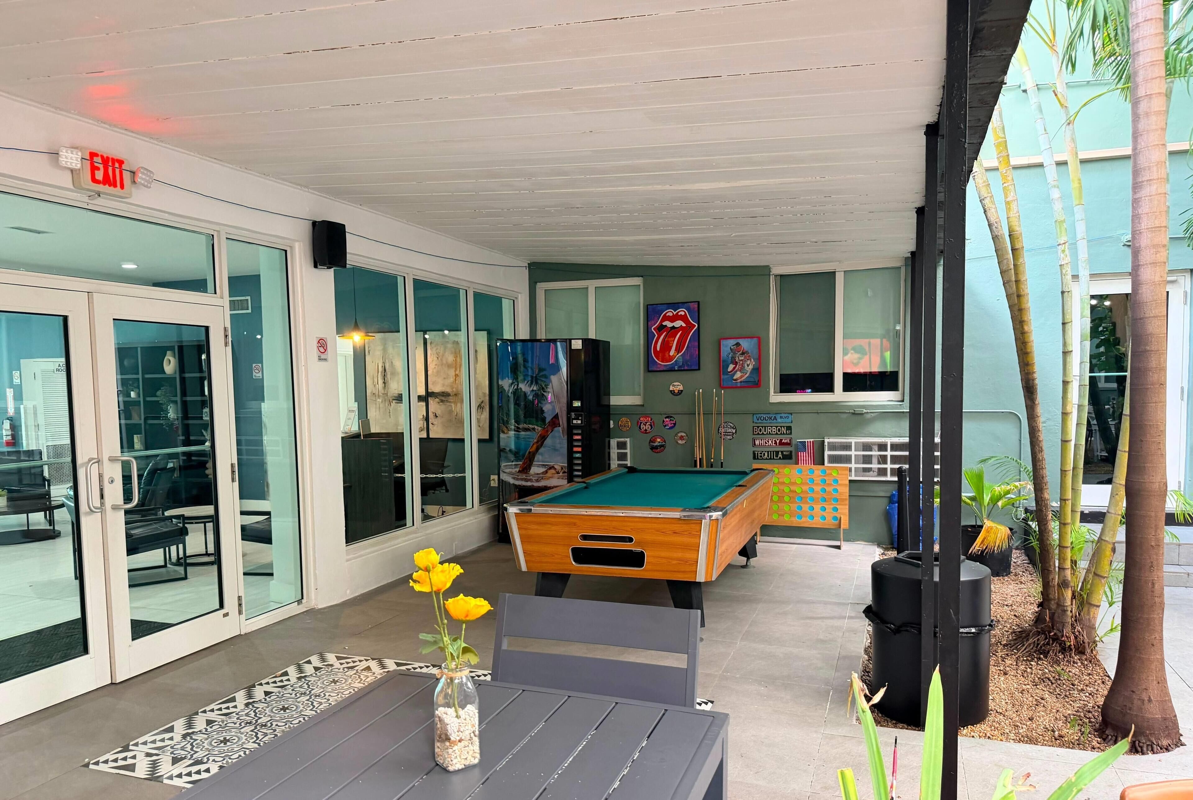 An indoor pool area with a pool table, a vase with yellow flowers, and a wall with various signs.