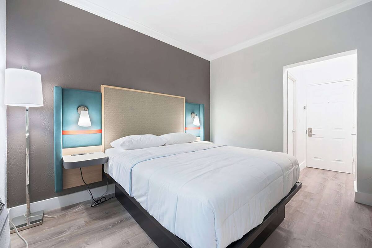Una moderna camera d'albergo con un letto grande, lampade ai comodini, una scrivania e una porta.