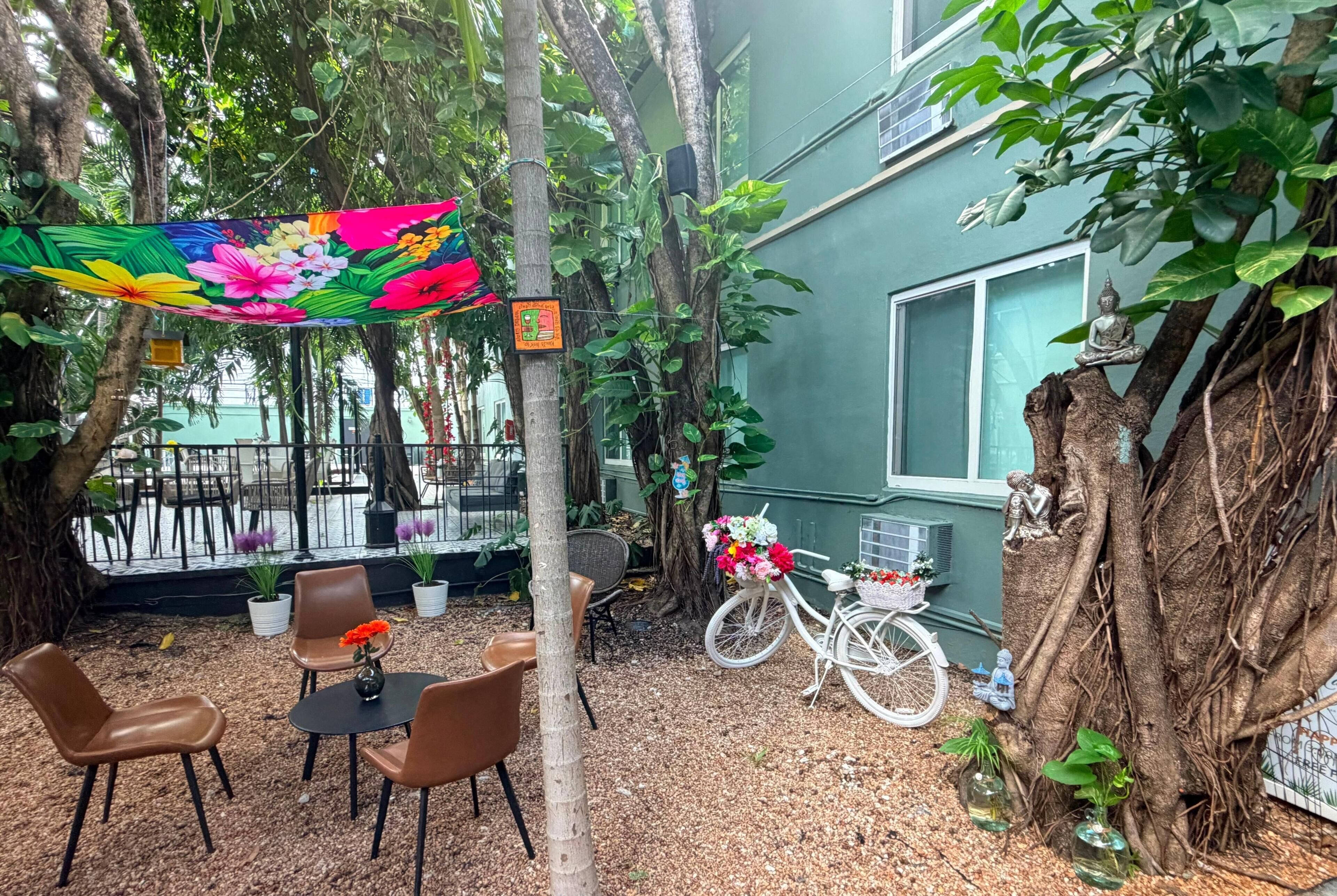 Un espacio al aire libre con sillas y una mesa, rodeado de árboles y plantas.