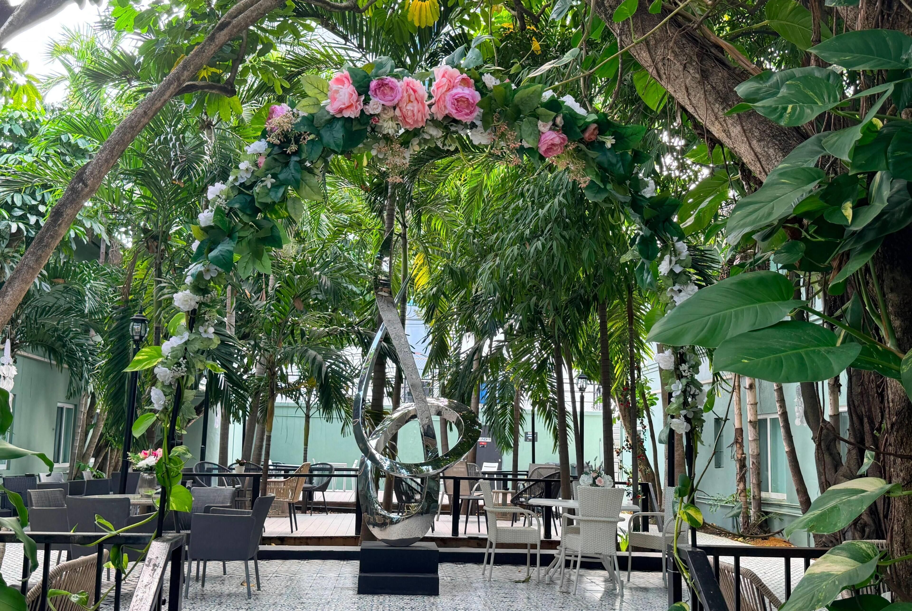 Un espace extérieur aménagé avec des tables et des chaises, entouré d’une végétation luxuriante et de plantes en fleurs.