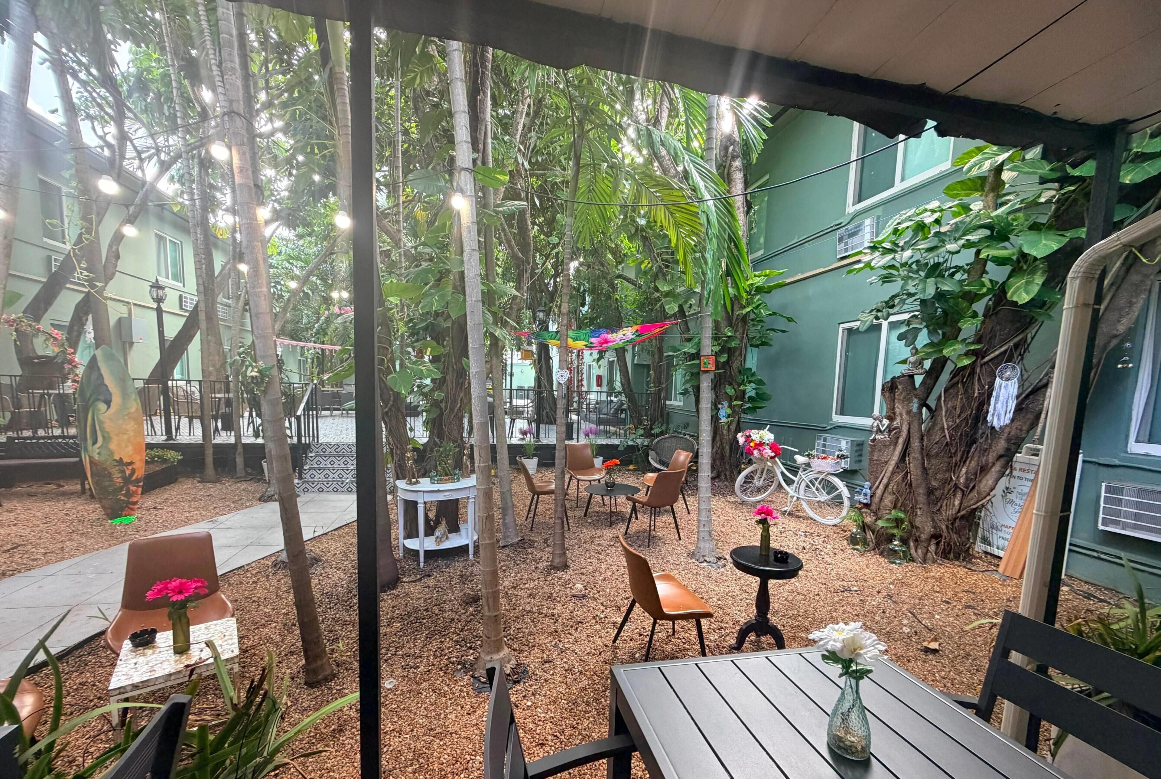 An outdoor seating area with tables and chairs, surrounded by trees and plants.