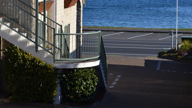 A building with a staircase leading to a balcony overlooking a body of water and mountains. - Colonial Lodge Motel (Taupo)