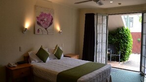 A bedroom with a bed, bedside tables, a ceiling fan, a window, and a door leading to an outdoor area. - Colonial Lodge Motel (Taupo)