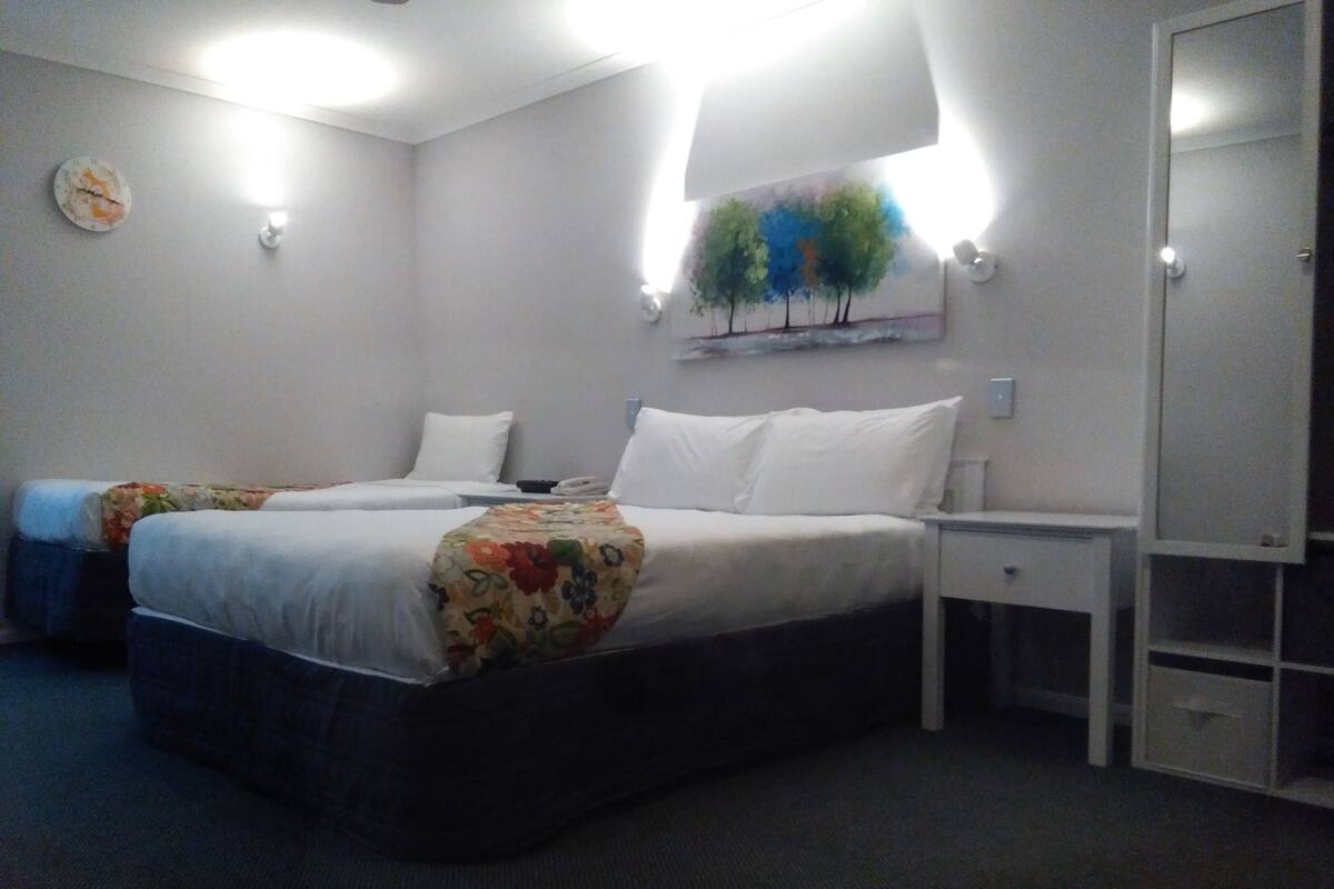 A hotel room with two beds, a nightstand, a dresser, and a painting on the wall.