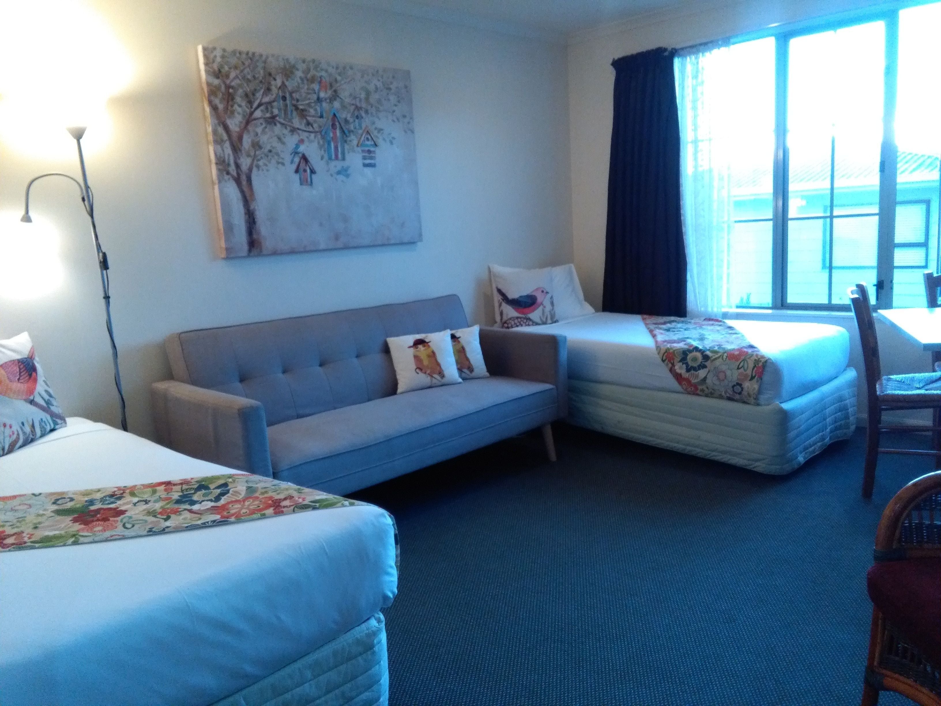 Een hotelkamer met een bank, twee éénpersoonsbedden, een stoel, een tafel en een raam met gordijnen.