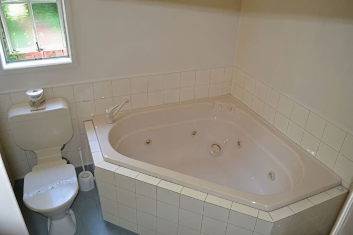 A bathroom with a bathtub, toilet, and a window.
