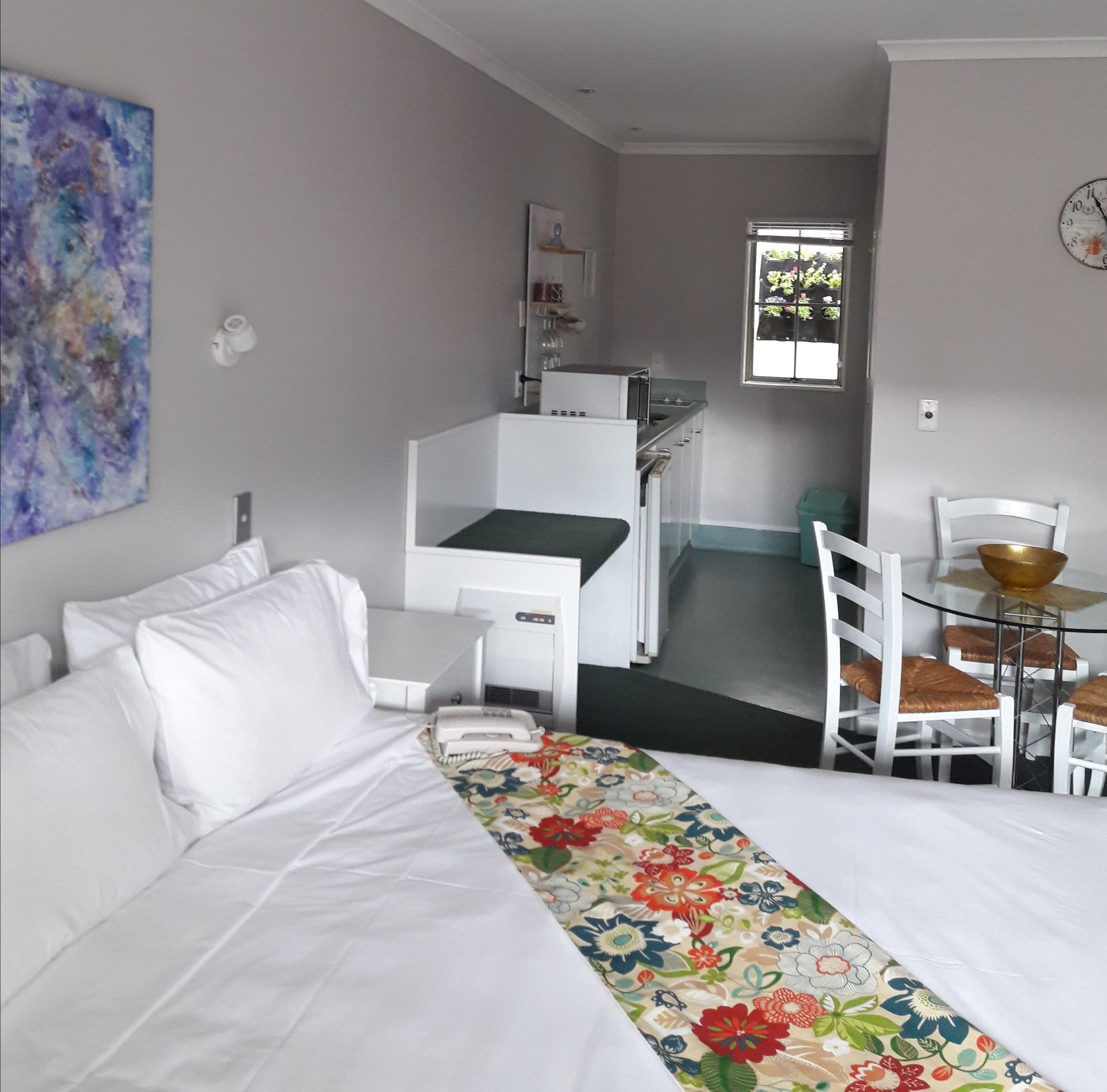 A room with a bed, a small kitchenette, a dining area with a table and chairs, and a window with a view.