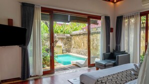 Un dormitorio con cama, televisor, piscina y vistas a un jardín.