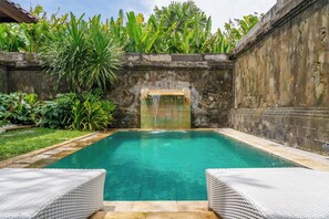 A rectangular pool with a waterfall feature, surrounded by lush greenery and stone walls.