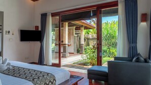 Un dormitorio con cama, sofá, televisor y puerta corrediza de vidrio que da a un patio con plantas.