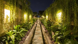 Un sendero nocturno bordeado de exuberante vegetación e iluminado por luces suaves, que conduce a una estructura distante.
