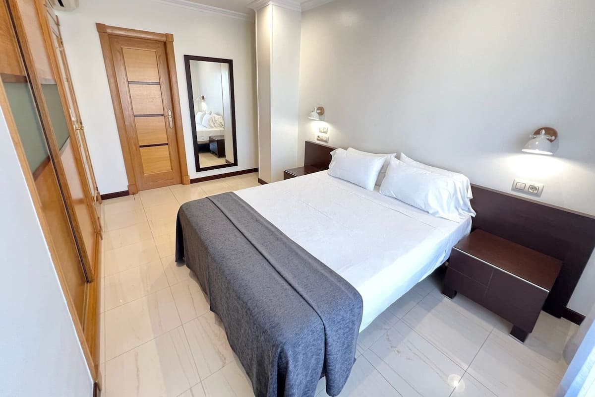 A hotel room with a large bed, bedside tables, a wardrobe, and a mirror.