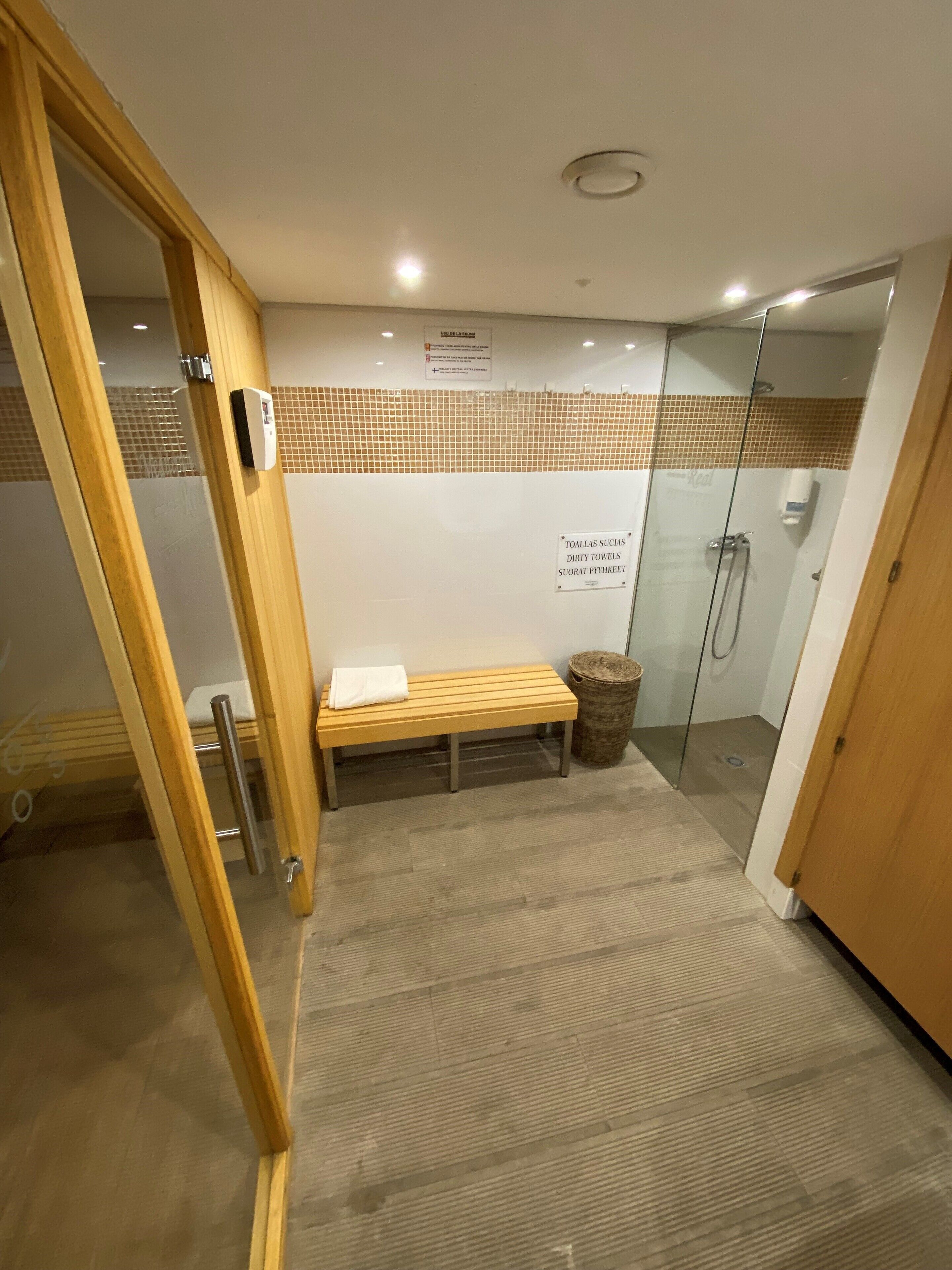 Zona de duchas públicas con un banco, un cubo de basura y una puerta de cristal.