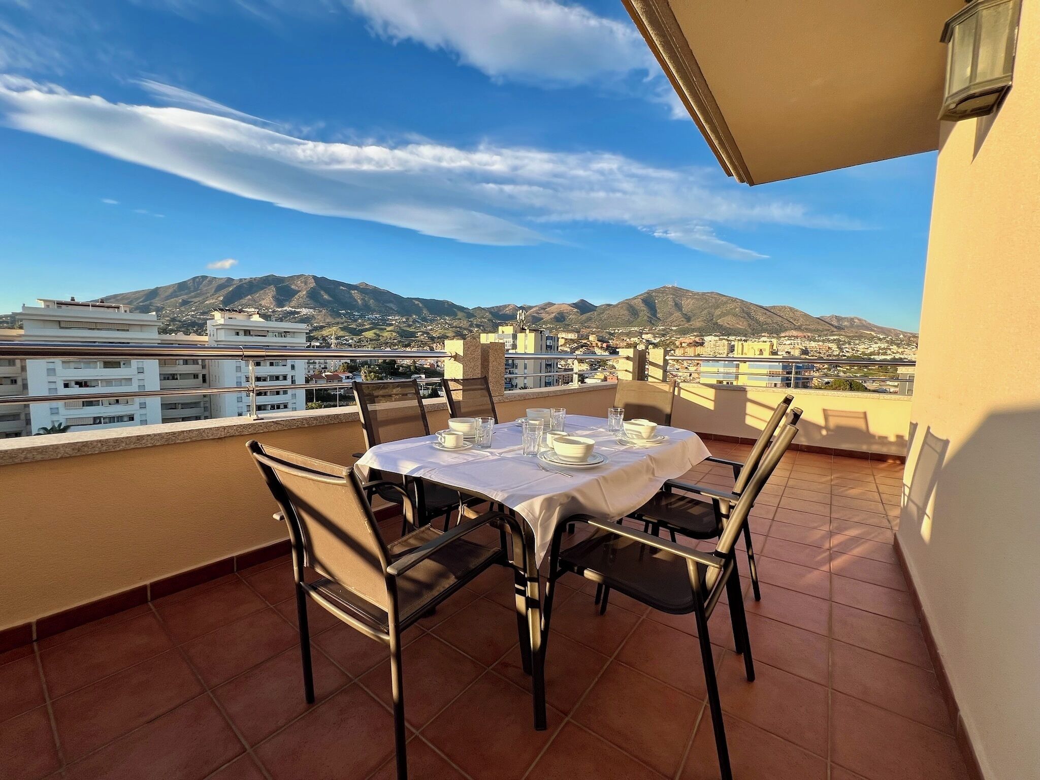 Una terraza con una mesa lista para comer, con vistas a un paisaje urbano y montañas.