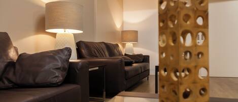 A modern living room with a brown leather sofa, two lamps, and a wooden decorative piece.