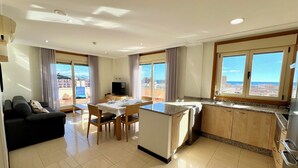 A modern hotel room with a dining area, kitchen, and a balcony with a city view. - Mediterraneo Real Apartamentos Turísticos (Fuengirola)