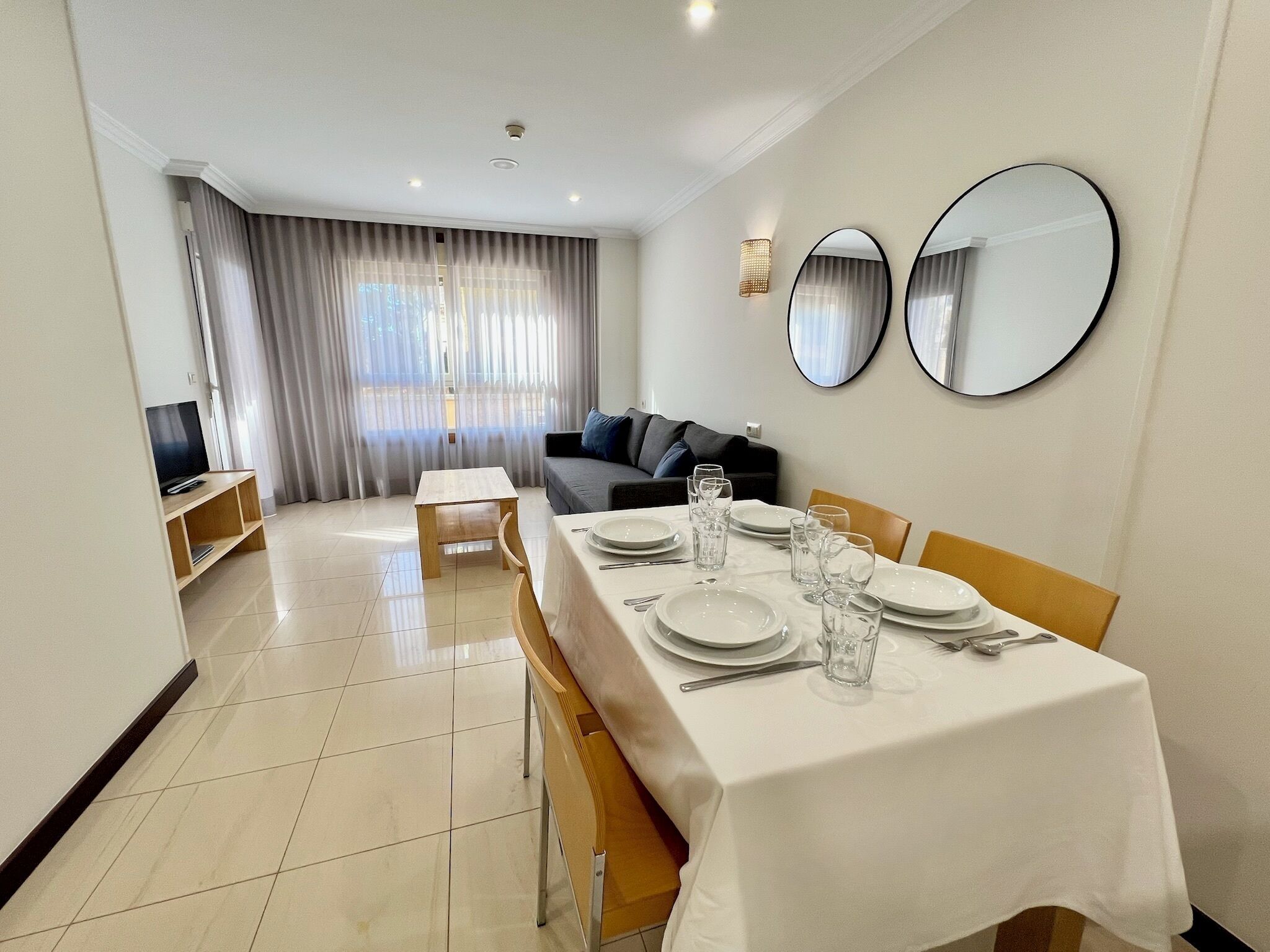 A modern dining area with a table set for four, a sofa, and a TV in the background.