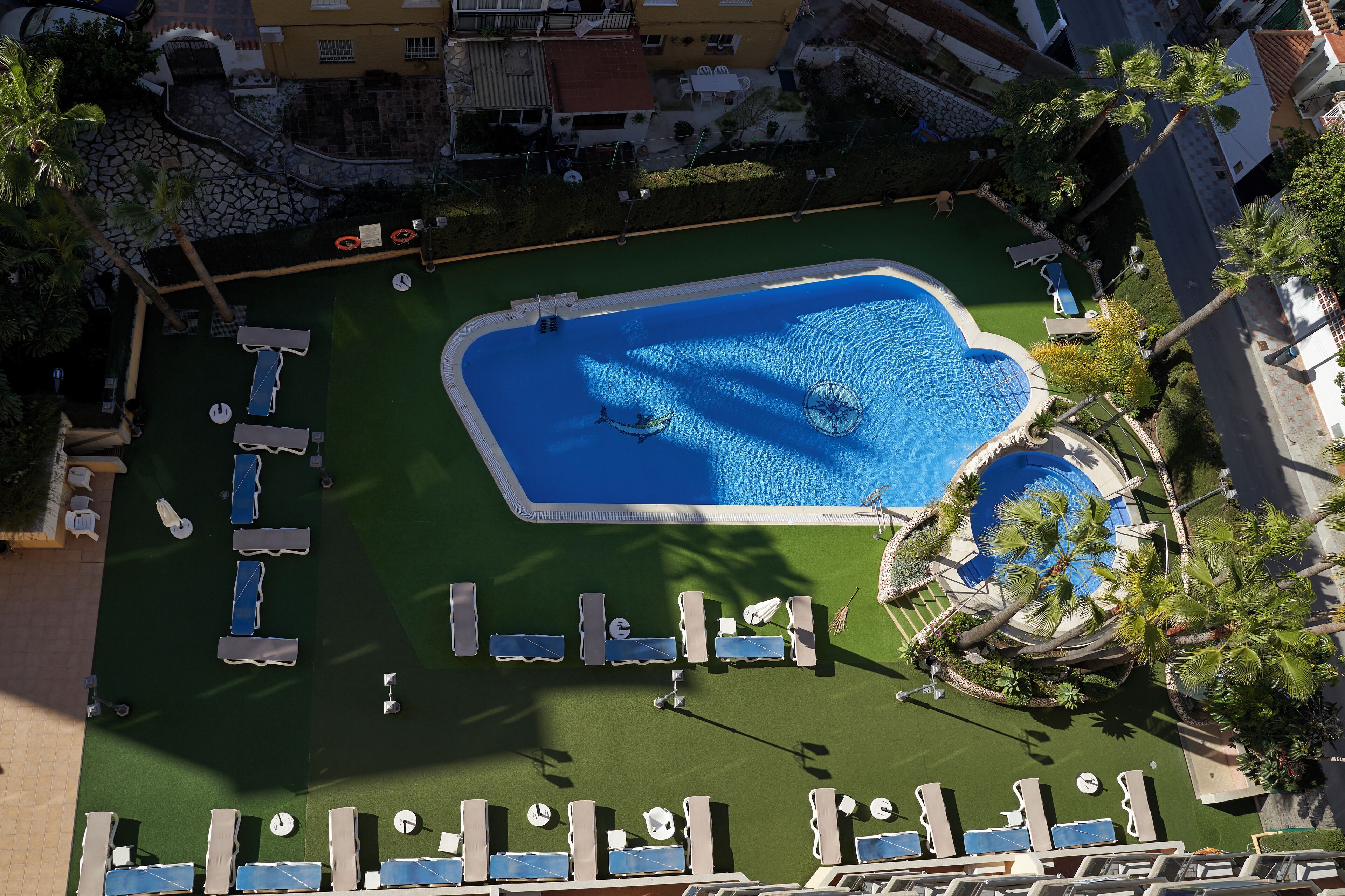 Vue aérienne d’un complexe hôtelier avec une piscine, des chaises longues et des palmiers.