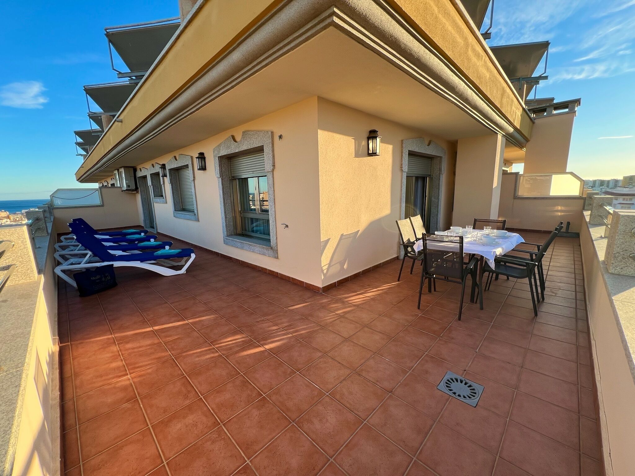 Une terrasse sur le toit avec une table et des chaises pour prendre les repas, une chaise longue et une vue sur la mer.