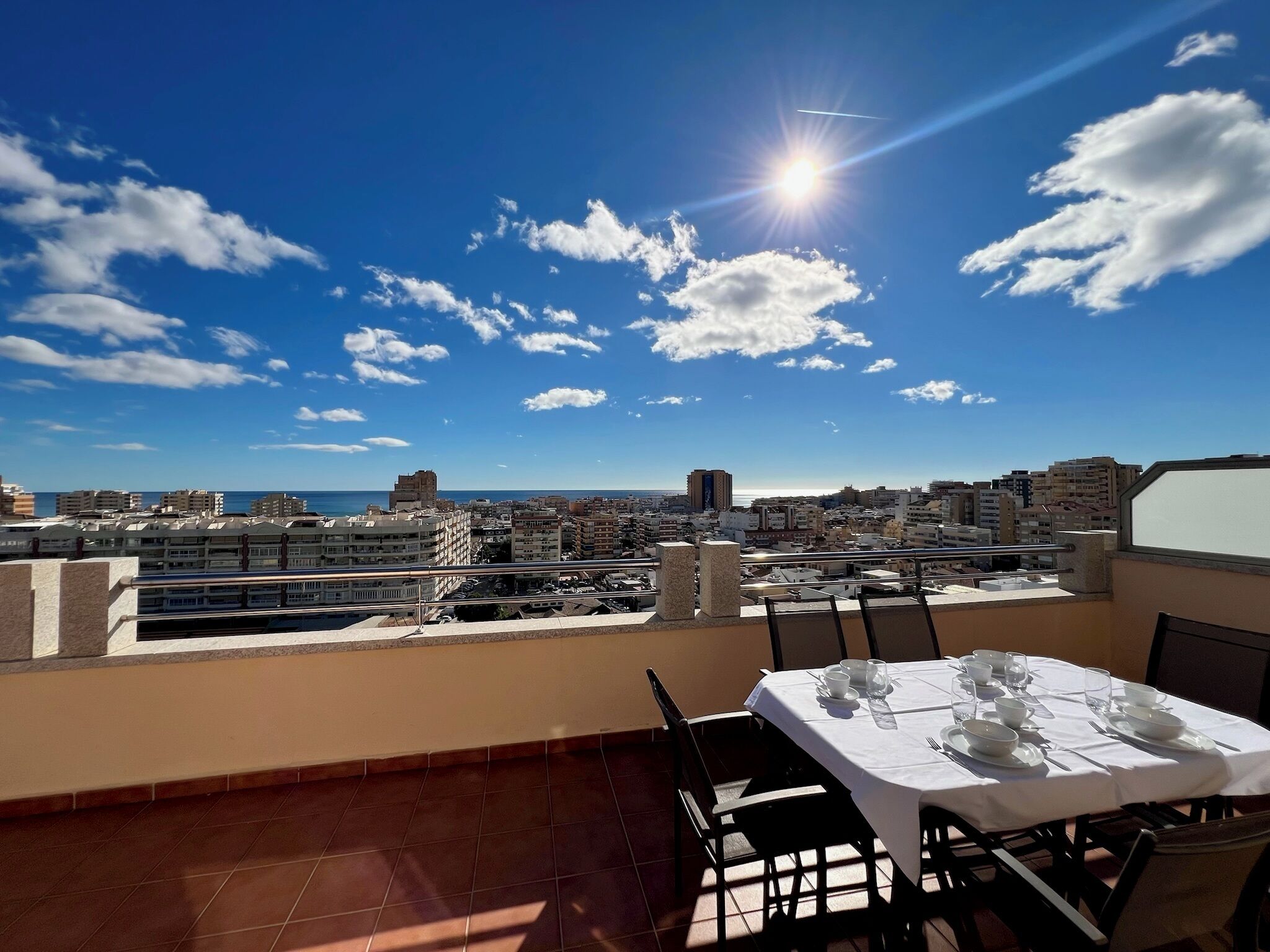 A rooftop terrace with a dining table set for four, overlooking a cityscape and the sea.