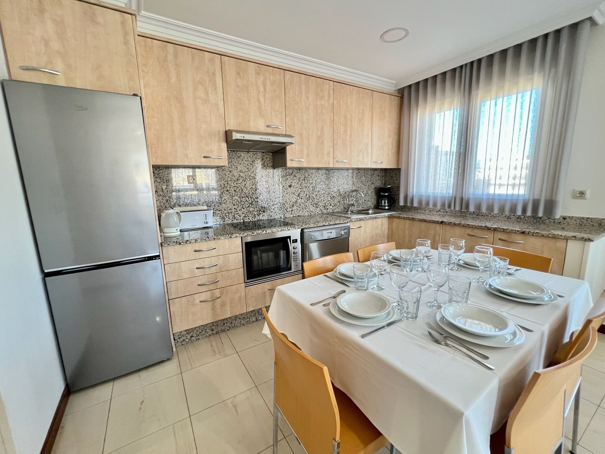 A modern kitchen with granite countertops, wooden cabinets, and a dining area set for six.