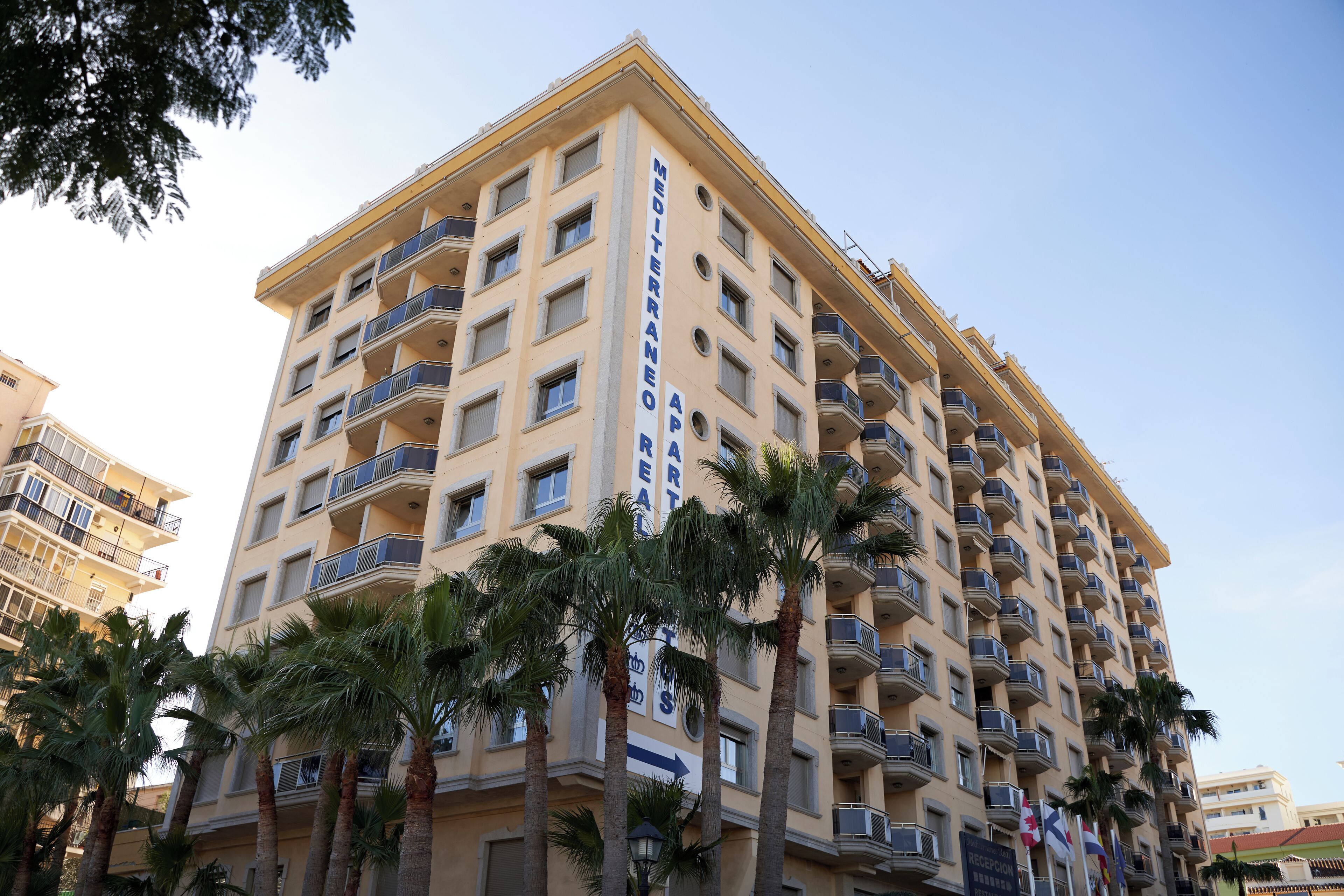 Un hôtel à plusieurs étages doté de balcons, de palmiers et surplombant un ciel dégagé.