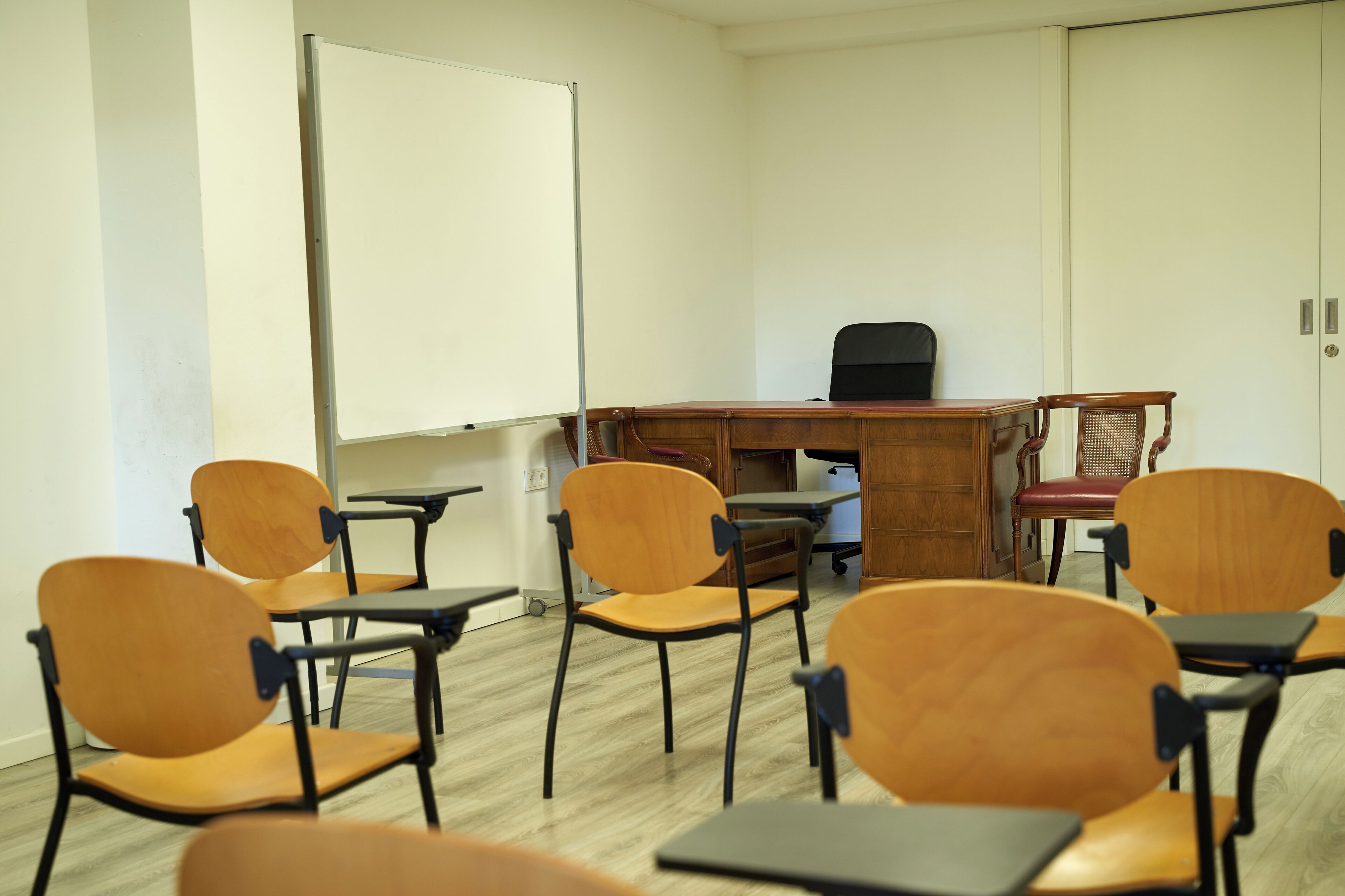 Ein Klassenzimmer mit Holztischen, Stühlen und einer Whiteboard-Tafel.