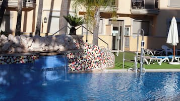 Una piscina al aire libre, sombrillas, sillones reclinables de piscina