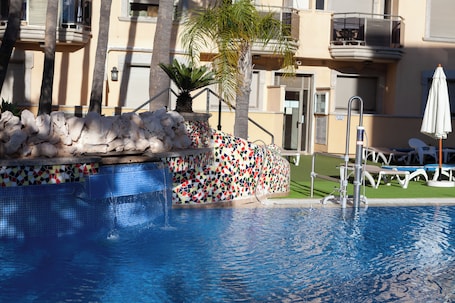 Una piscina al aire libre, sombrillas, sillones reclinables de piscina